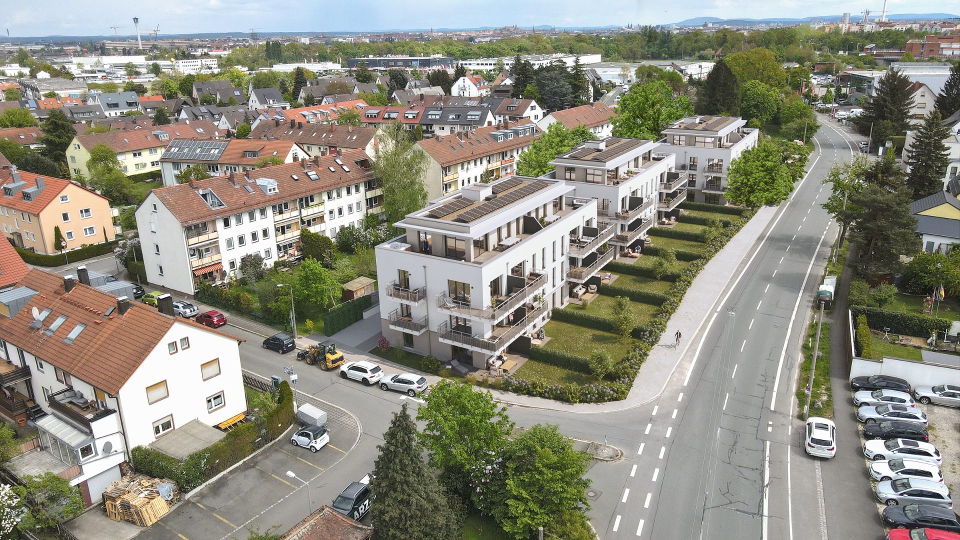 Mehrfamilienhäuser mit Solarpaneelen und Gärten; Umgebung mit Straßen und anderen Gebäuden.